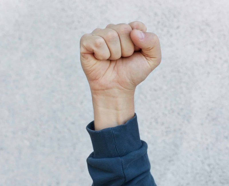 Unknown person protesting, activist fist up during strike. Activism for equal human rights or against racism, faceless human upraising fist isolated over white background.