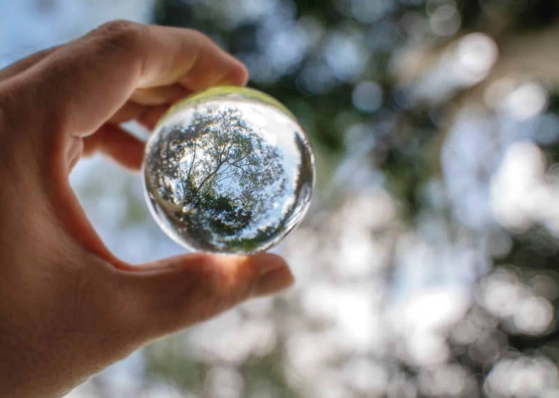 Reflection of blue sky, white clouds and trees in a glass ball in holding hand
